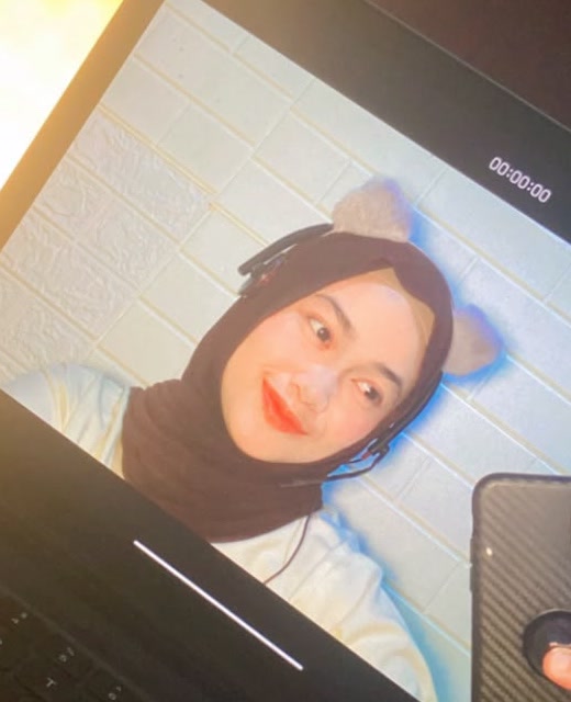 Teacher Dila smiling on camera in her online classroom with a headset